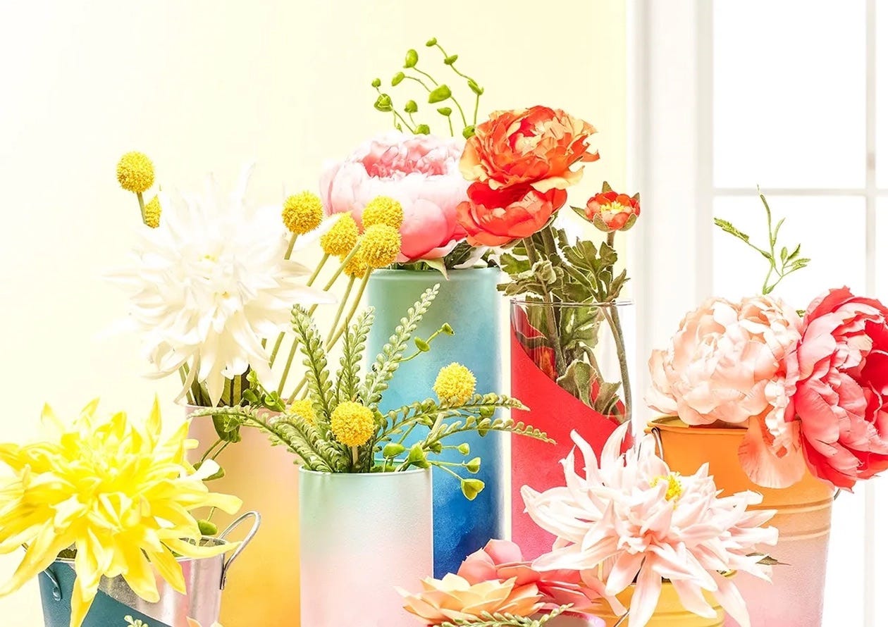 Delta Creative-painted vases with ombre gradients, holding colorful artificial flowers and greenery.